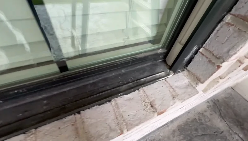 Construction dust and mortar residue around a dark window frame before final detailing